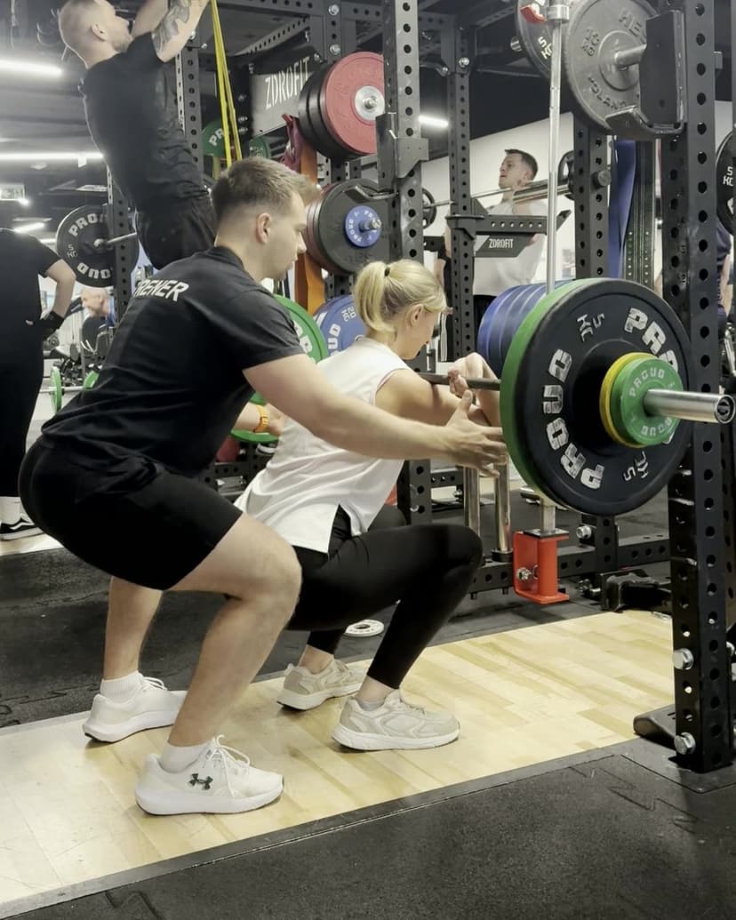 Daniel Przybysz spotting a client during a barbell squat at a gym in Gdańsk
